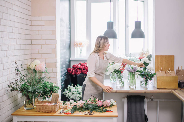 Smiling lovely young woman florist arranging plants in flower shop - Foto, Imagen