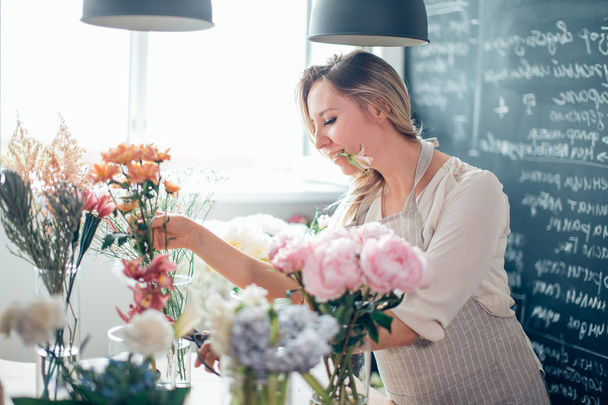 Smiling lovely young woman florist arranging plants in flower shop - Fotó, kép