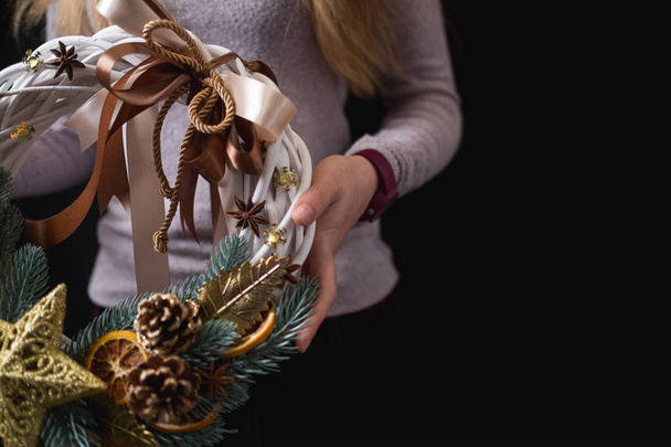 close-up of female hands holding Christmas wreath on black background - 写真・画像