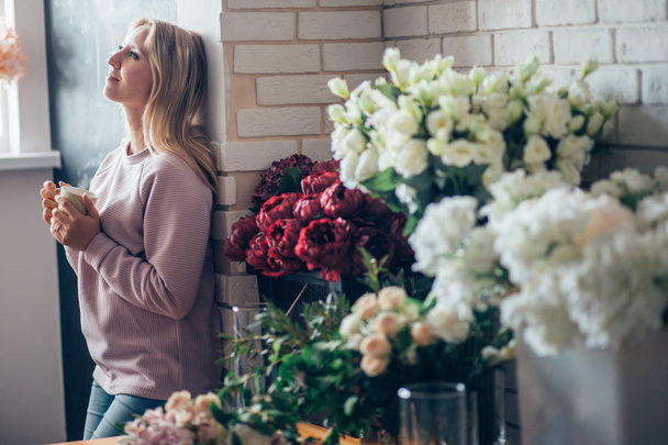 Florist woman in process of making bouquet, holds in her hand a cup of coffee - Фото, зображення