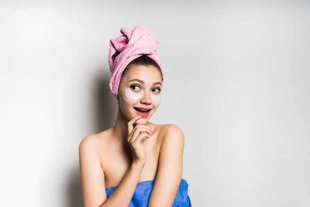 attractive shining girl with a pink towel on her head, cleverly smiles, under the eyes of silicone patches - Fotografie, Obrázek