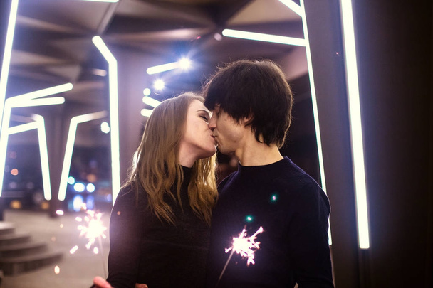 Lifestyle portrait of couple in love holding sparkling New Year fireworks on the city streets with lot of lights on background. New year and Christmas celebration concept. - Photo, Image