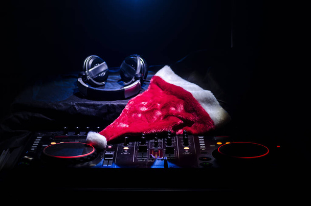 Mélangeur DJ avec écouteurs sur fond de boîte de nuit sombre avec sapin de Noël Nouvel An. Vue rapprochée des éléments ou symboles du Nouvel An (Santa Clause, Bonhomme de neige, Chien 2018, coffret cadeau) sur une table Dj. tonique
 - Photo, image