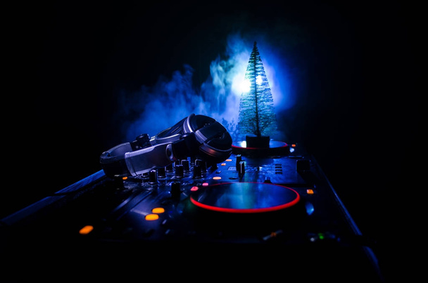 Μείκτης για DJ με ακουστικά σε φόντο σκοτεινό νυχτερινό κέντρο διασκέδασης με Χριστουγεννιάτικο δέντρο το νέο έτος Eve. Κλείνω πάνω θέα του έτους νέα στοιχεία ή σύμβολα (Άγιος Βασίλης, χιονάνθρωπος, σκύλου 2018, κιβώτιο δώρων) σε έναν πίνακα του Dj. ήπια - Φωτογραφία, εικόνα