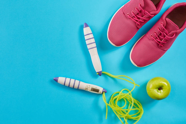 Flat lag van vrouwelijke sport apparatuur in roze kleur met springtouw en sneakers op blauwe achtergrond - Foto, afbeelding