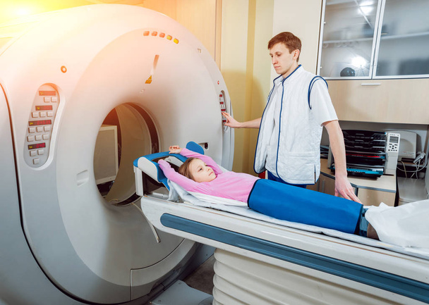 Equipo médico. Médico caucásico masculino y paciente niña en sala de tomografía computarizada en el hospital
. - Foto, Imagen