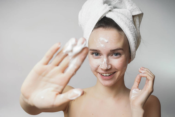 funny woman in a towel on the head happy cleanses the skin with foam on a white background isolated. Skincare cleansing concept - Foto, immagini