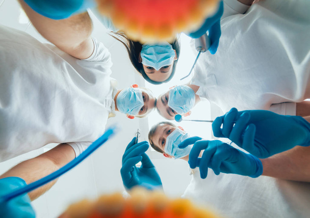 Four dentist in uniform perform dental implantation operation on a patient at dentistry office - 写真・画像