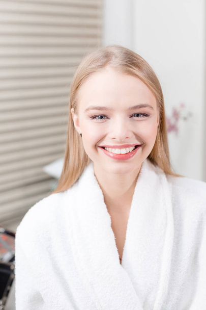 Porträt einer attraktiven lächelnden blonden Frau. im weißen Bademantel nach dem Eingriff. Kosmetologie und Wellness-Center-Konzept. - Foto, Bild