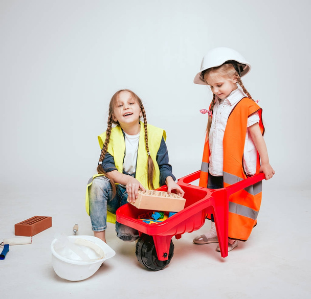 Two little cheerful girls with braids playing in repair or construction on white - 写真・画像