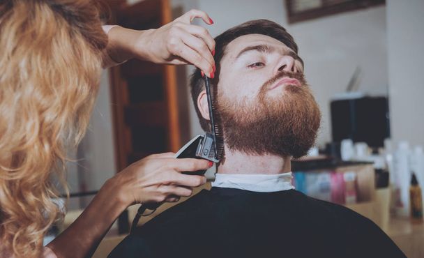 Master leikkaa hiukset ja parta miesten, kampaaja tekee kampauksen nuorelle miehelle
. - Valokuva, kuva