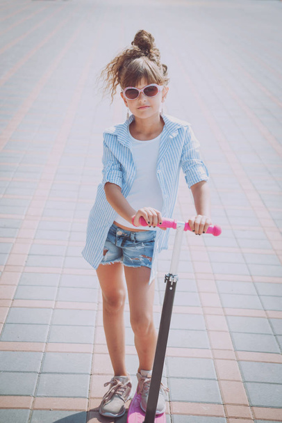Little girl riding scooter on the street at sunny day - Fotoğraf, Görsel