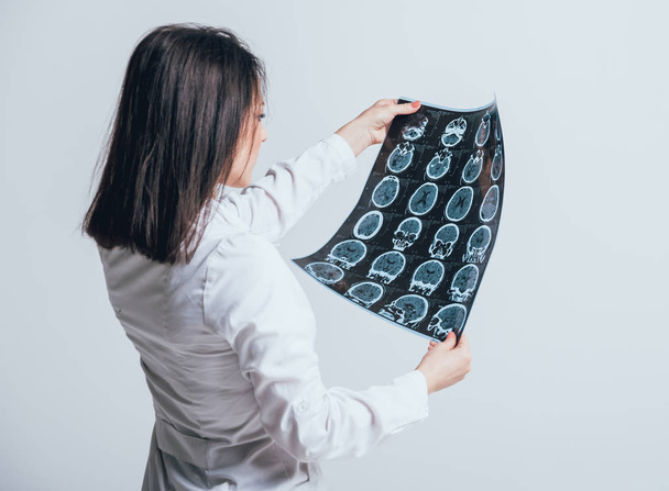 Female doctor attentively examines the MRI scan before white wall - Fotó, kép