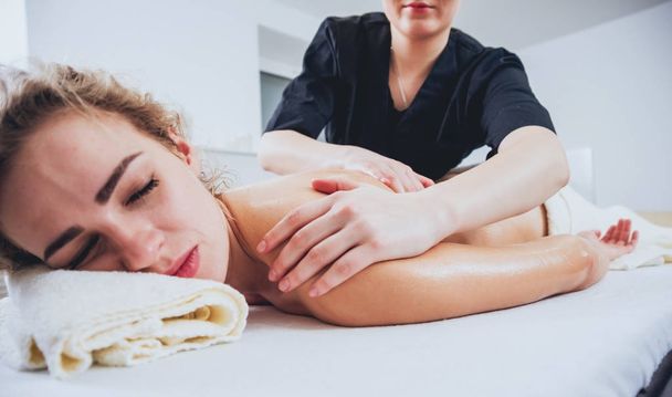 Young curly caucasian girl relaxing in spa. Body massage. - Фото, изображение