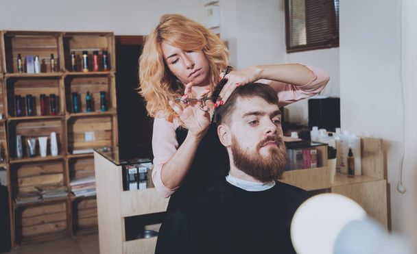 Master cuts hair and beard of men, hairdresser makes hairstyle for a young man. - Foto, Imagen