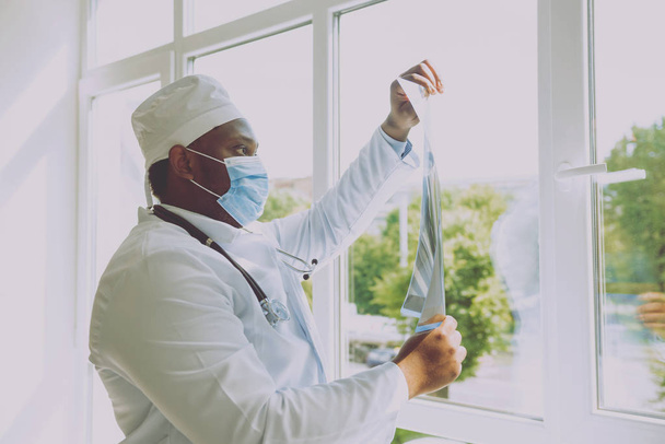 African american doctor looking at x-ray film in hospital room near window - Фото, зображення