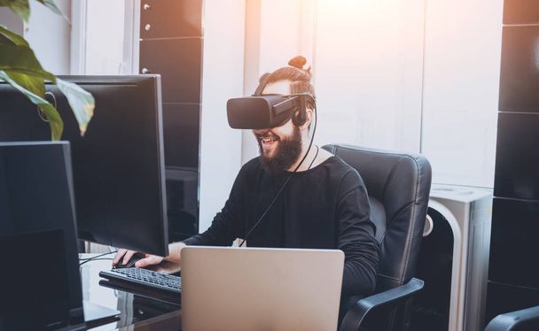Young man with beard wearing virtual reality goggles at the office - Foto, Bild