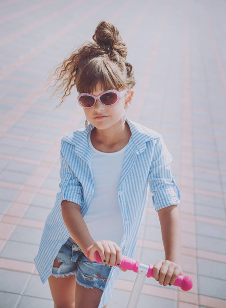 Little girl riding scooter on the street at sunny day - Фото, изображение