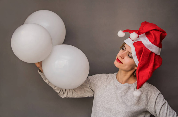 Noel Baba şapkaları gri arka plan ağaç beyaz balonlarla genç Avrupa kadın - Fotoğraf, Görsel