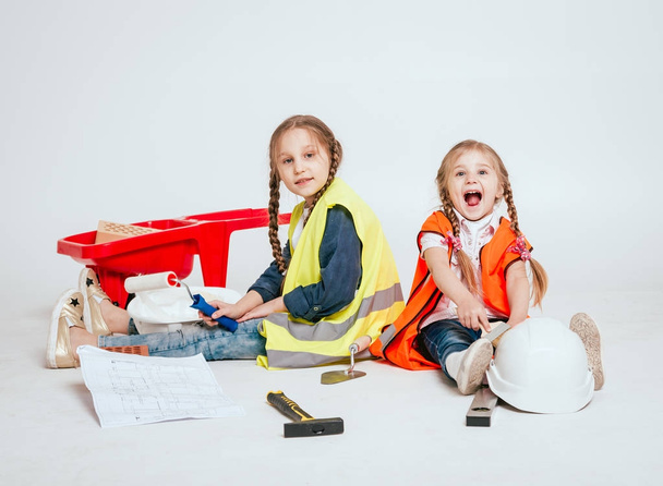 Two little cheerful girls with braids playing in repair or construction on white - Фото, изображение