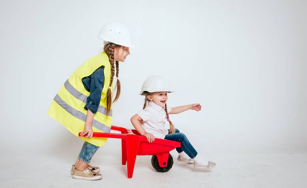 Дві маленькі веселі дівчата з косами грають у ремонті або будівництві на білому
 - Фото, зображення