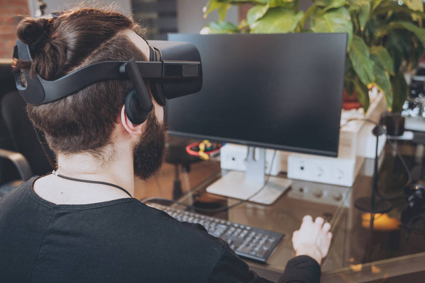 Young man with beard wearing virtual reality goggles at the office - Foto, imagen
