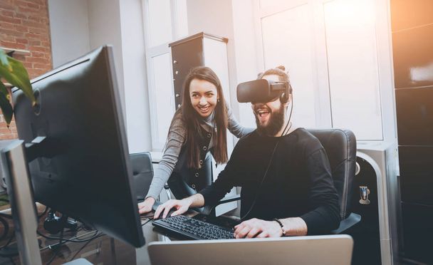 Young man with woman creative office workers testing VR goggles and having fun - 写真・画像