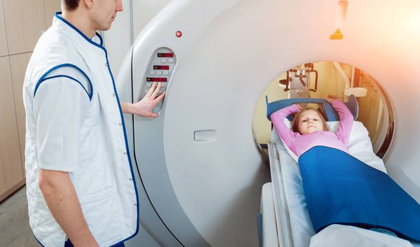 Medical equipment. Male caucasian doctor and little girl patient in room of computed tomography at hospital. - Photo, image