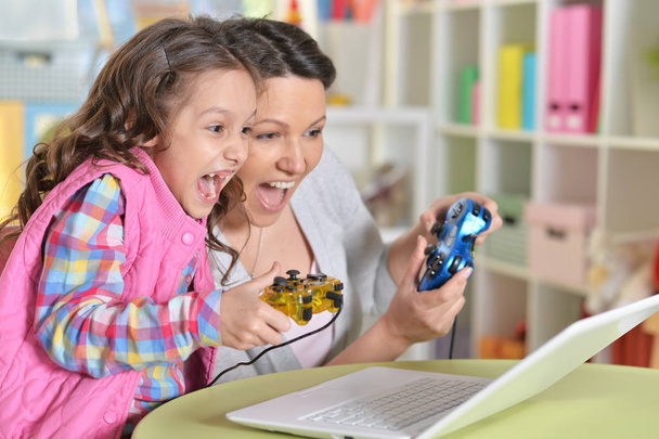 Portret van gelukkige moeder en dochter speelspel op laptop - Foto, afbeelding