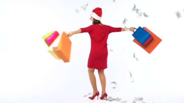 Dollar bills falling on Christmas shopping woman with multicolored shopping bags and crazy dancing on white background in studio. Lets go holiday shopping concept. Slow motion - Кадри, відео