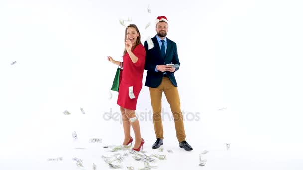 Dollars falling on formally dressed man and woman in the Santa Claus hat. Lets go holiday shopping and celebrate concept. Slow motion - Felvétel, videó