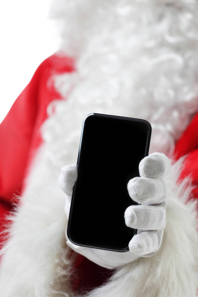 Christmas concept shot with Santa holding a black smart phone, showing it into the camera - Φωτογραφία, εικόνα