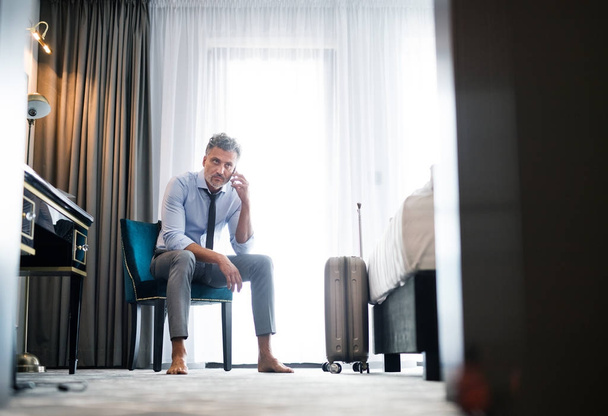 Mature businessman with smartphone in a hotel room. - Foto, Bild