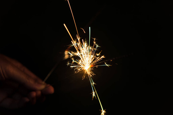 Female hands holding sparkler with night background - Foto, afbeelding