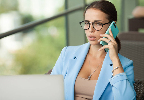 Woman working on laptop at office while talking on phone - Photo, image