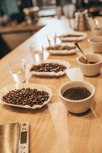 Close-up van gearrangeerde kommen met koffiebonen en vermalen koffie voor voedsel functie op houten tafelblad - Foto, afbeelding