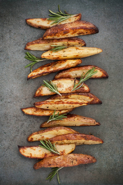 Slices of baked potatoes with rosemary on a textured stone table - 写真・画像