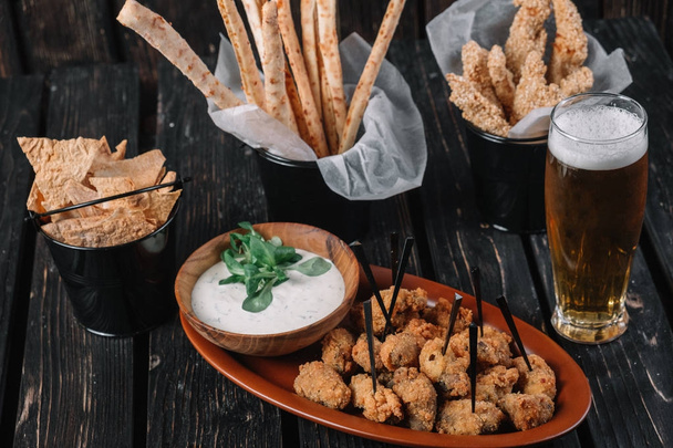 Glass of beer and snacks on dark wood background. Grissini, chicken grilled breast, pita chips - Photo, Image