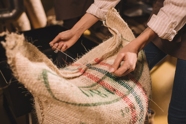 partial view of worker tying sack bag with coffee beans - Фото, зображення