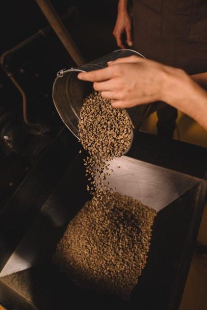 visão parcial do torrador de café derramando grãos de café na máquina de torrefação
 - Foto, Imagem