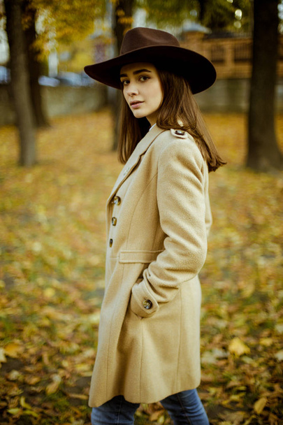 Attractive young woman in fashionable hat posing in autumnal park  - Fotó, kép