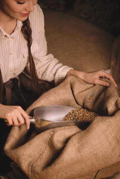 vista parcial del trabajador recogiendo granos de café con cucharada de metal de la bolsa de saco
 - Foto, Imagen