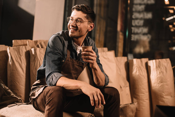 glimlachend koffie rooster met kop koffie pauze hebben tijdens werk - Foto, afbeelding