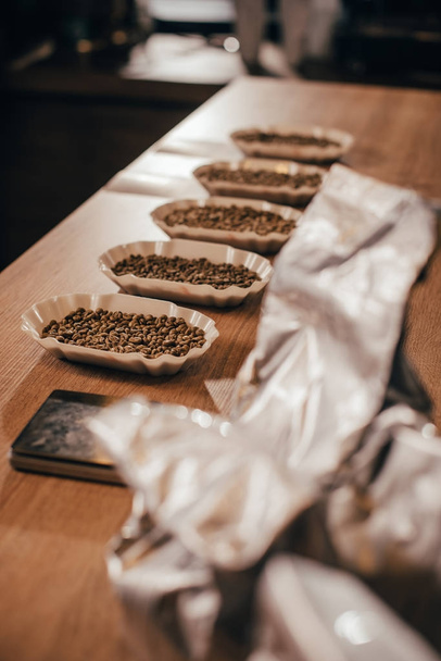 Close-up van gearrangeerde kommen met koffiebonen voor voedsel functie op houten tafelblad - Foto, afbeelding