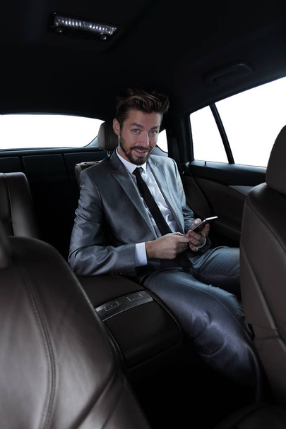 man in pak zitten in auto en lezen van berichten op smartphone - Foto, afbeelding