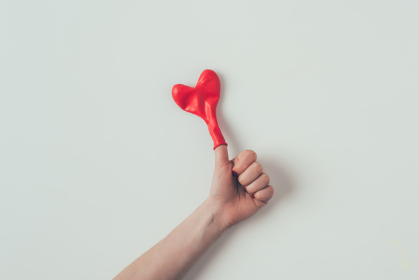 cropped image of woman showing thumb up with heart shaped balloon on finger on white, valentines day concept - Foto, afbeelding