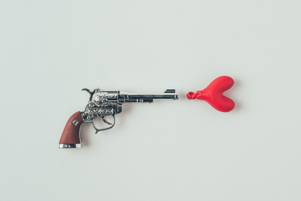 bovenaanzicht van pistool gericht op hartvormige ballon geïsoleerd op wit, Valentines Day concept - Foto, afbeelding