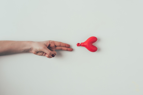 cropped image of woman reaching out deflated balloon with two fingers on white, valentines day concept - Fotó, kép
