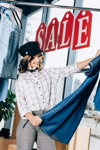 mujer joven con estilo mirando el vestido de mezclilla azul en la tienda de ropa
 - Foto, Imagen