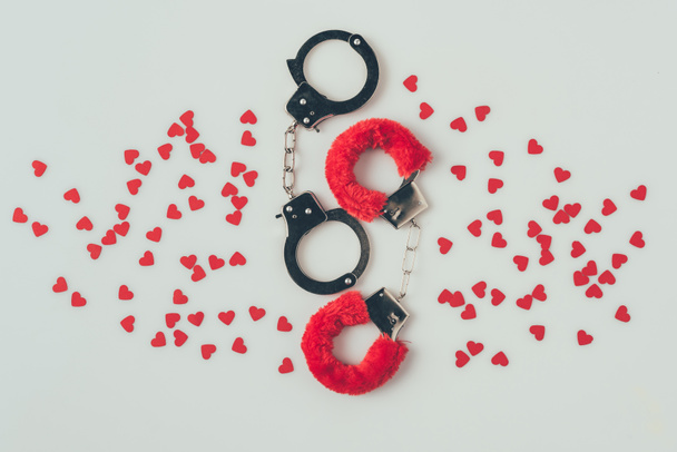 top view of black and red handcuffs with scattered paper hearts isolated on white, valentines day concept - Photo, Image